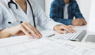 (c) Leonardo da/Shutterstock.com Ärztin vor PC und Befunden des Patienten