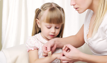 (c) Sergey Nivens/Shutterstock.com Mutter klebt ein Pflaster auf den Arm ihrer jungen Tochter